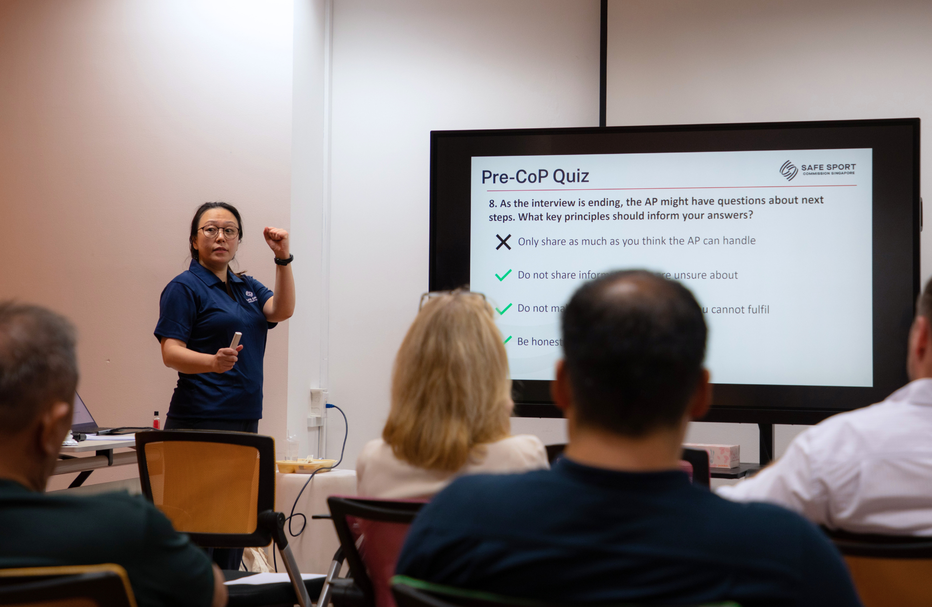 A woman stands in front of a screen displaying a presentation titled "Pre-CoP Quiz" while several people sit in the audience.